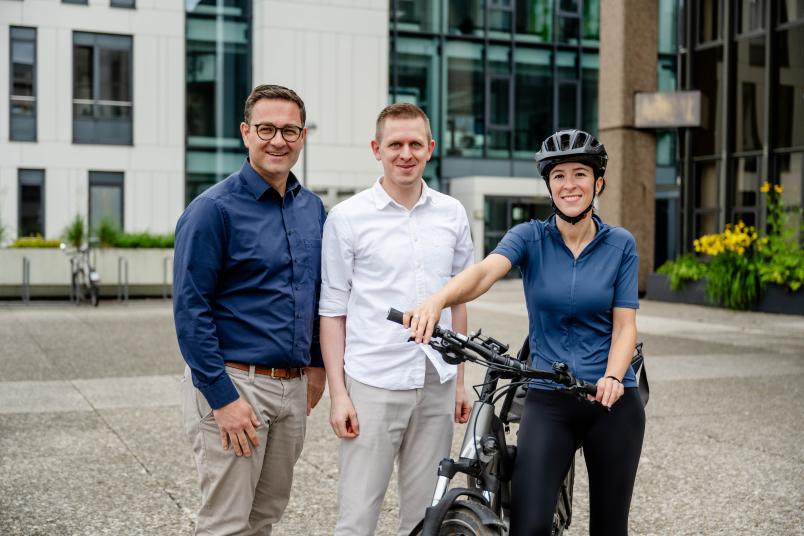 drei Menschen, eine Fahrradfahrerin darunter