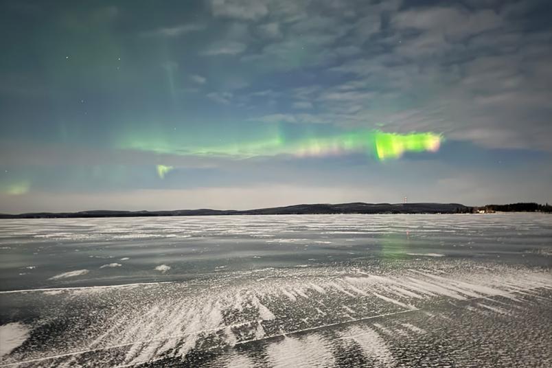 Polarlichter in grün und gelb am Himmel über einem schneebedeckten Boden. 