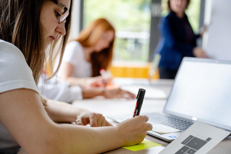 Studentin schreibt mit einem Stift auf Papier. 