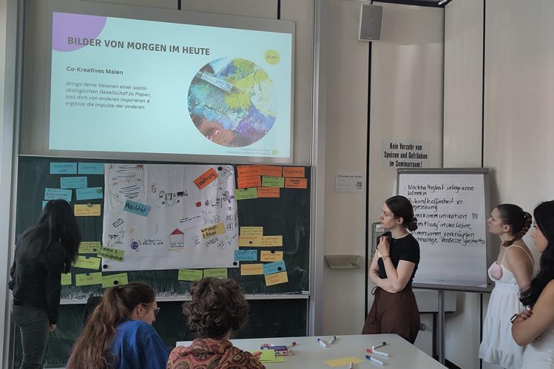 Studierene in einem Seminarraum. An die Wand wird mit einem Beamer eine Präsentation geworfen. 