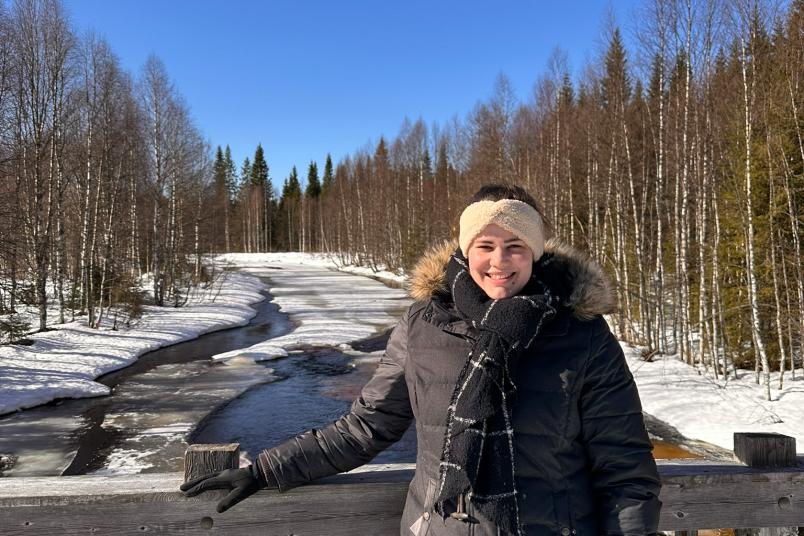 Studentin steht in Winterkleidung vor einem Fluss auf einer Brücke