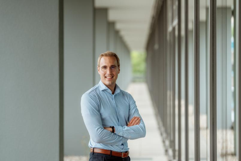 Porträt eines jungen, schlanken Mannes im hellblauen Hemd und mit blonden kurzen Haaren und Brille.