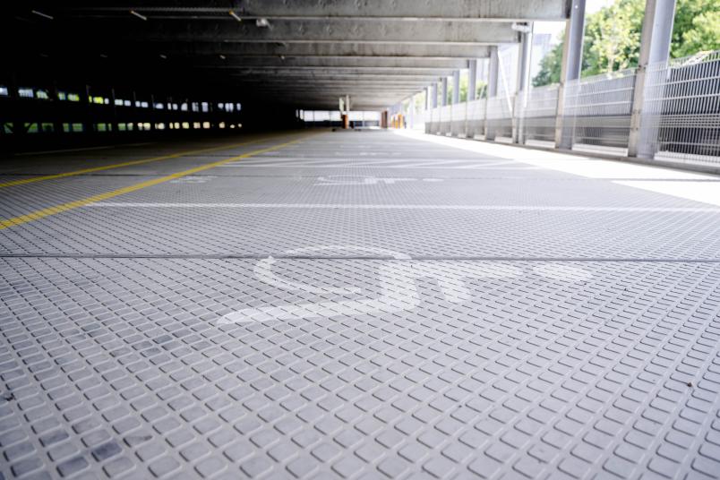 Das Foto zeigt ein leeres Parkhaus von innen. Auf dem Boden mit weißer Farbe ein Behindertenparkplatz markiert.
