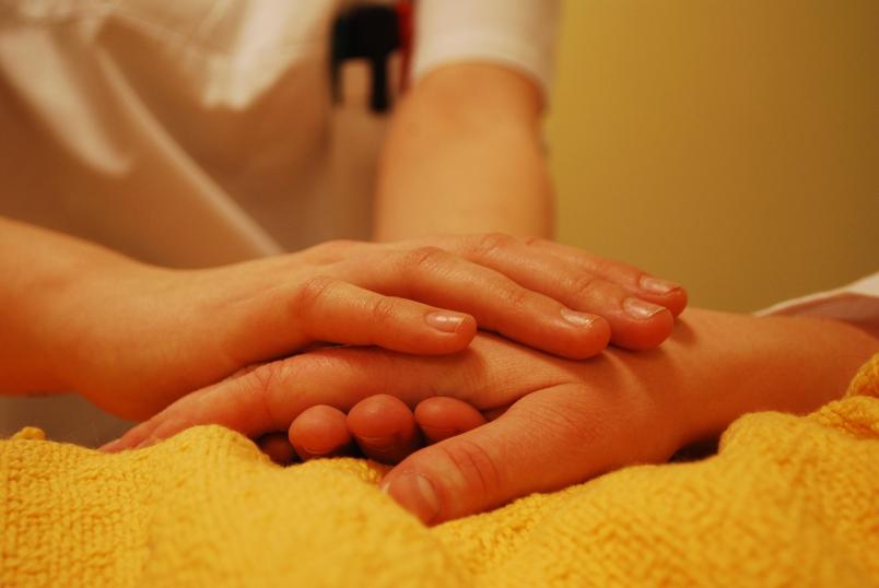 Eine Frau hält die auf einer Decke liegende Hand einer Person. 