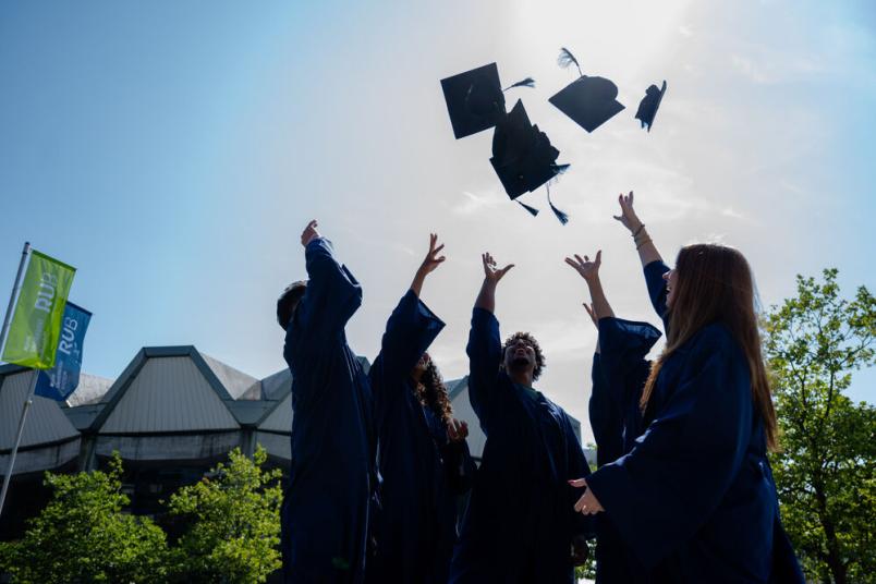 Studierende werfen Doktorhüte in die Luft. 