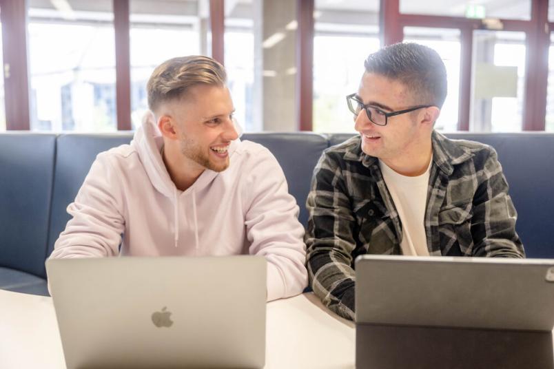 Zwei Studierende sitzen an ihren Laptops nebeneinander. 