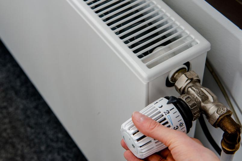 Eine Hand am Thermostat eines Heizkörpers