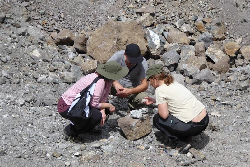 Drei Personen hocken in einer steinigen Landschaft