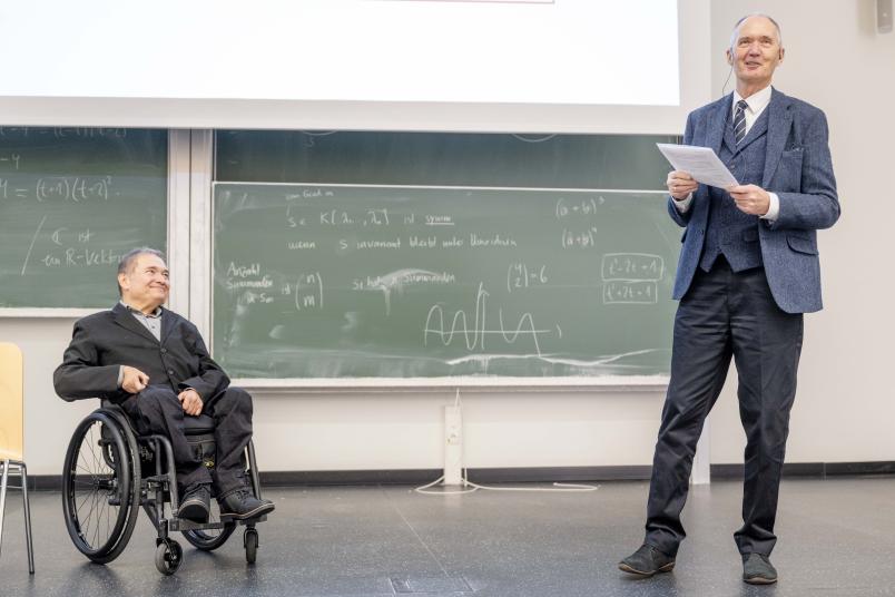 Zwei Männer vor Tafeln in einem Hörsaal