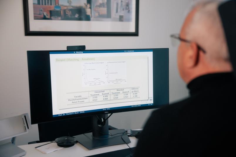 Mann von hinten schaut auf Bildschirm auf dem Statistiken zu sehen sind.