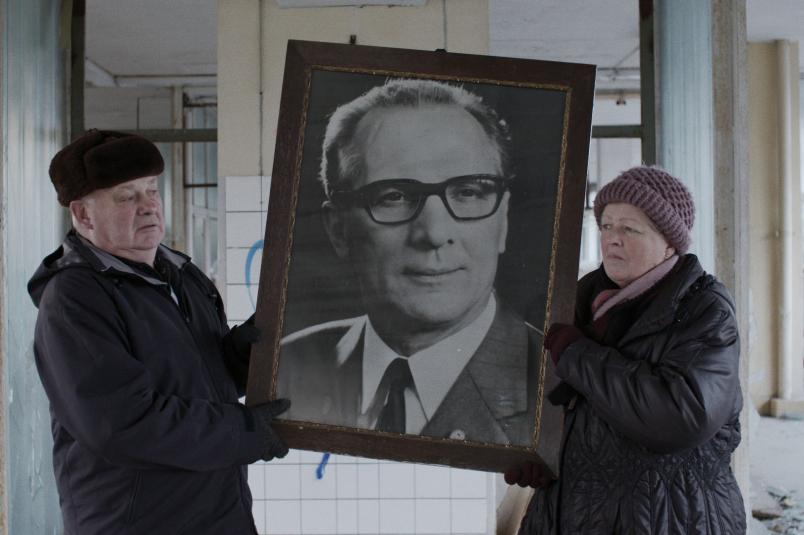 Eine Frau und ein Mann halten ein großes Foto von Erich Honecker