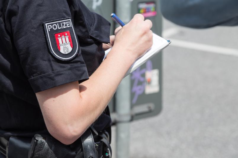 Polizist notiert Aussage. Man sieht seinen/ihren Kopf nicht, sondern nur den Oberkörper und den Notizblock.