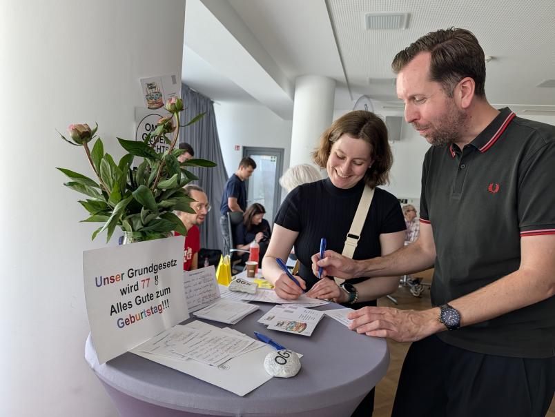 Zwei Personen schreiben an einem Stehtisch eine Postkarte