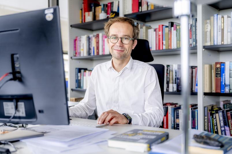 Porträt von Sören Urbansky am Schreibtisch, im Hintergrund ein großes Bücherregal