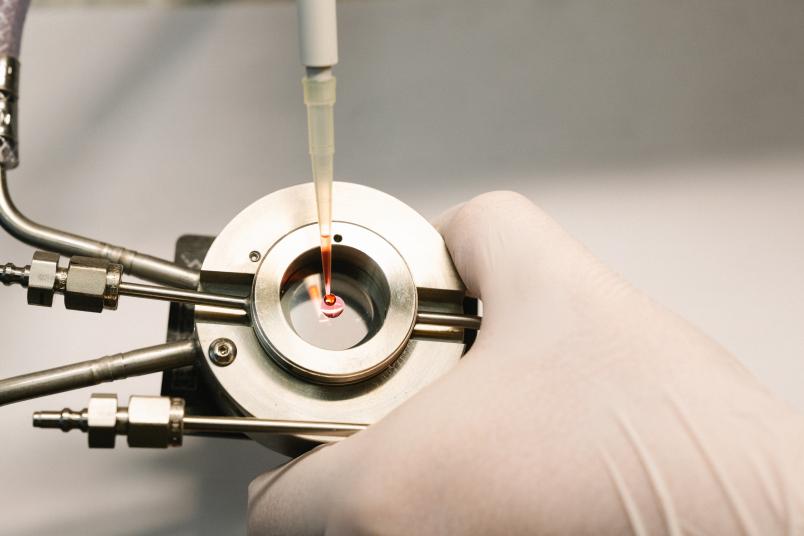 Eine runde Messzelle aus Metall, in die aus einer Pipette eine rote Flüssigkeit eingefüllt wird