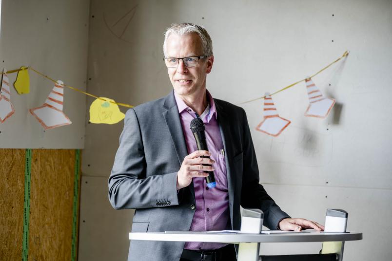 Robert Grosche von der RUB steht mit einem Mikrofon in der Hand an einem Rednerpult.