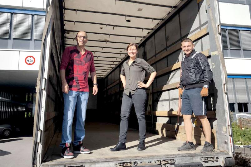 Gruppenbild von drei Personen auf der Laderampe des LKW.