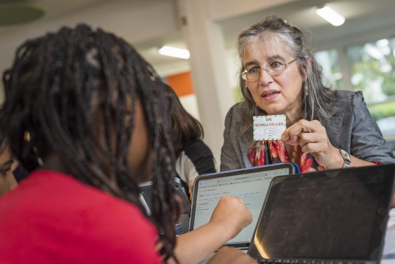 Karin Yesilada hält einem Kind eine Karte mit der Aufschrift "Die Schallwellen" hin