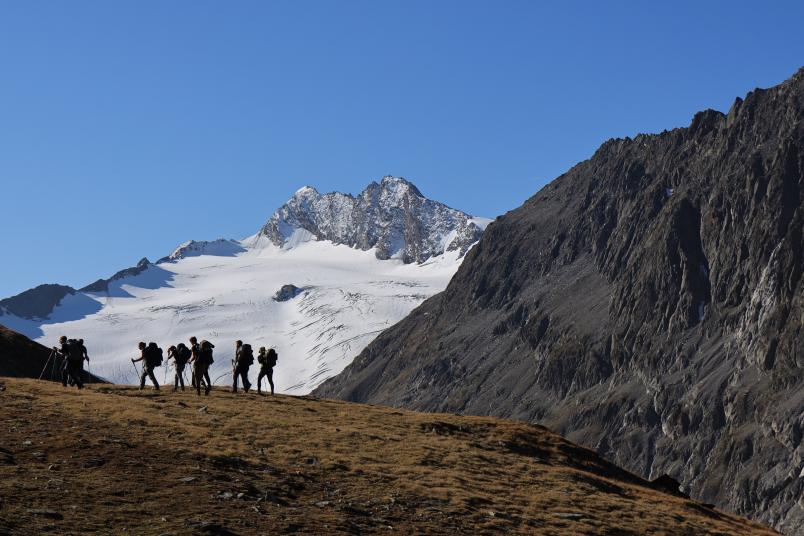 Eine Gruppe an jungen Leuten wandert. Im Hintergrund sind Berge zu sehen.