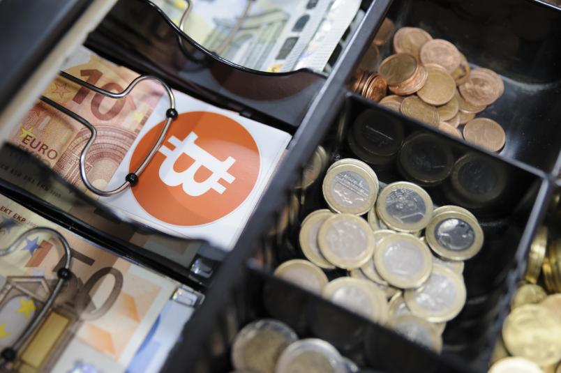 Kasse mit Euro-Münzen und -Scheinen und einem Bitcoin-Aufkleber