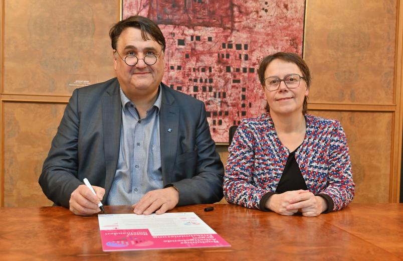 Rektor Martin Paul und Kanzlerin Christina Reinhardt sitzen an einem Tisch und unterzeichnen die Charta für die Ruhr-Universität Bochum.