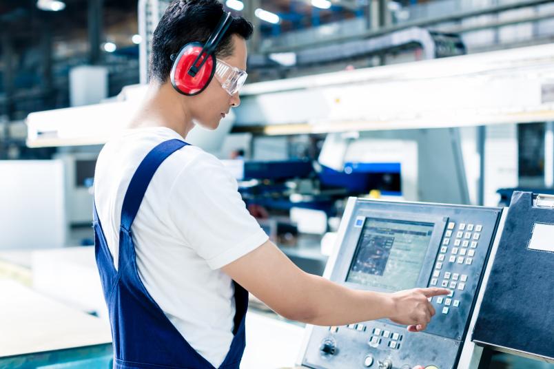 Ein Arbeiter gibt Daten an einer CNC-Maschine in einer Produktionshalle ein