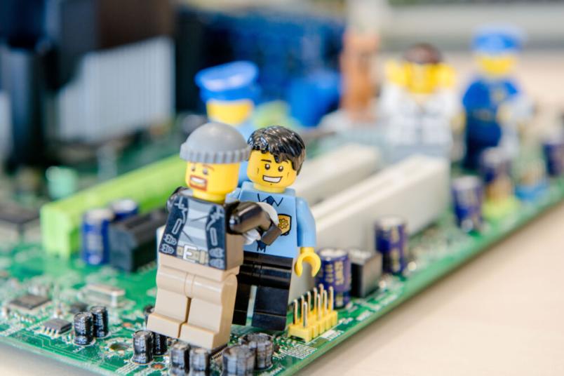 Ein Polizisten-Lego-Männchen nimmt ein Gauner-Lego-Männchen fest, während sie auf einer Computerplatine stehen.