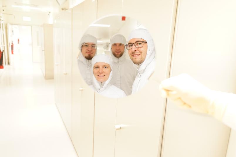 Die Köpfe von vier Personen in Schutzanzügen spiegeln sich in einer silbrigen Scheibe.