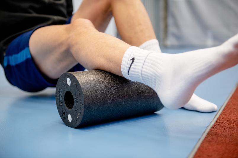 Sportler rollt Bein über eine Blackroll.