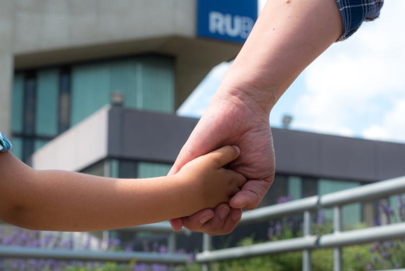 Kinderhand und Erwachsenenhand vor dem Musischen Zentrum der RUB