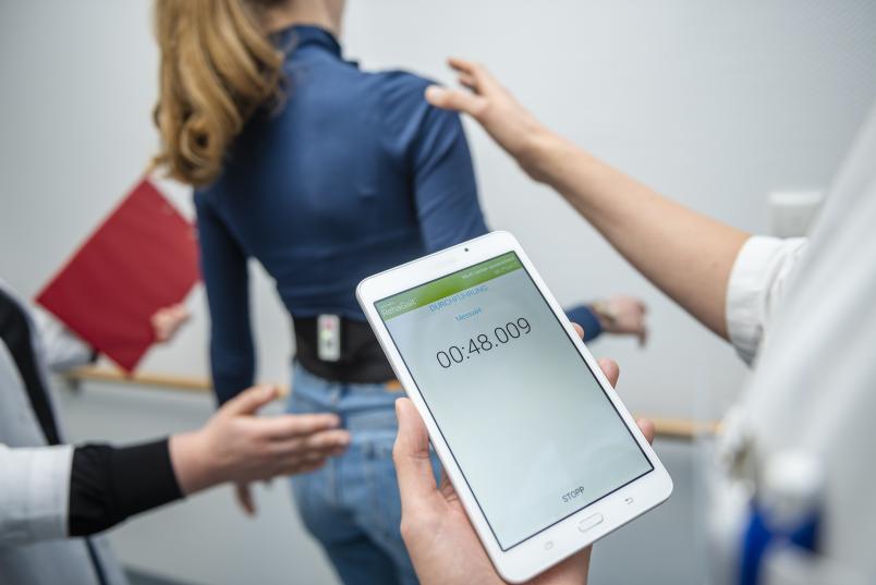 Hände halten Frau fest, die auf Balance-Board wackelig steht.