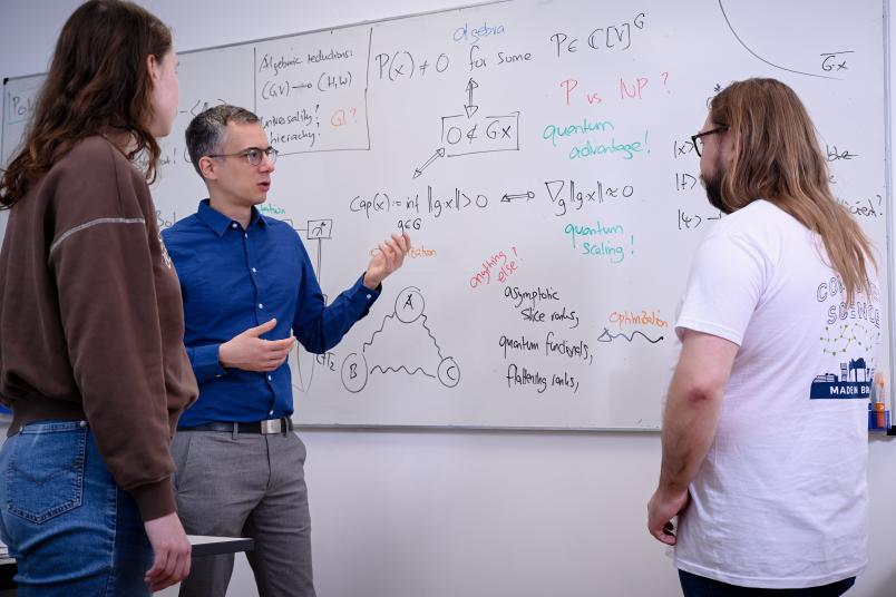 Drei Personen diskutieren über Formeln an einem Whiteboard.
