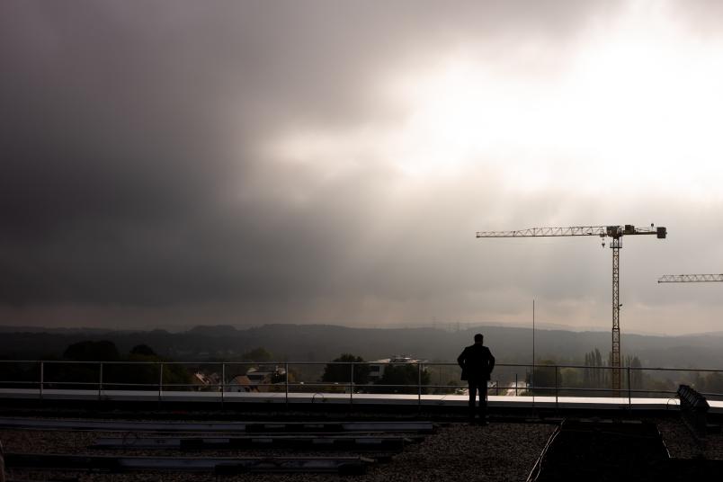Durch graue Wolken scheint die Sonne auf zwei Baukräne.