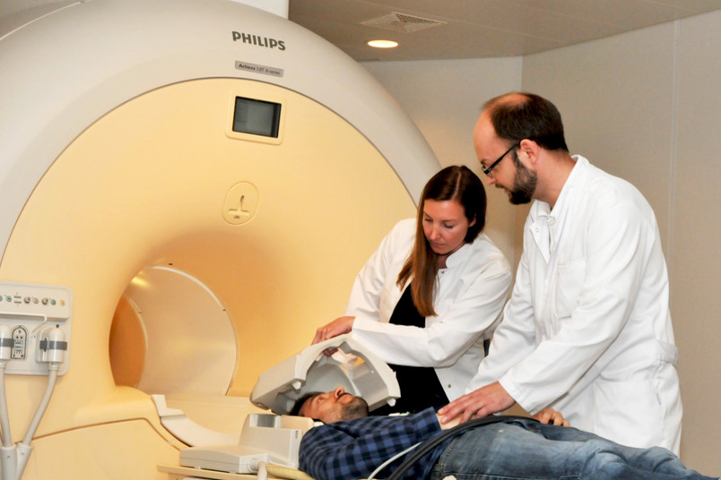Eine Frau und ein Mann in weißen Kitteln bereiten einen Patienten für eine Untersuchung im Kernspintomografen vor.