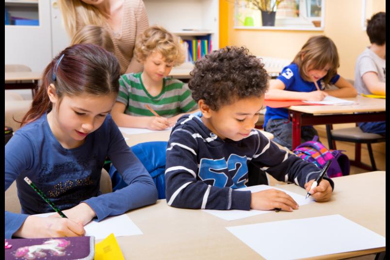 Kinder sitzen an einem Tisch und schreiben etwas in ihre Hefte.