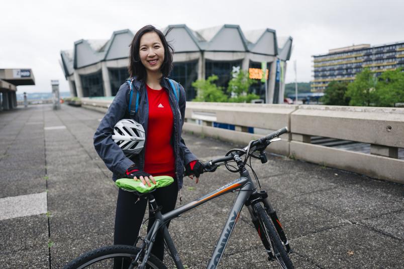 Junge Frau steht mit Fahrrad vor dem Audimax der RUB.