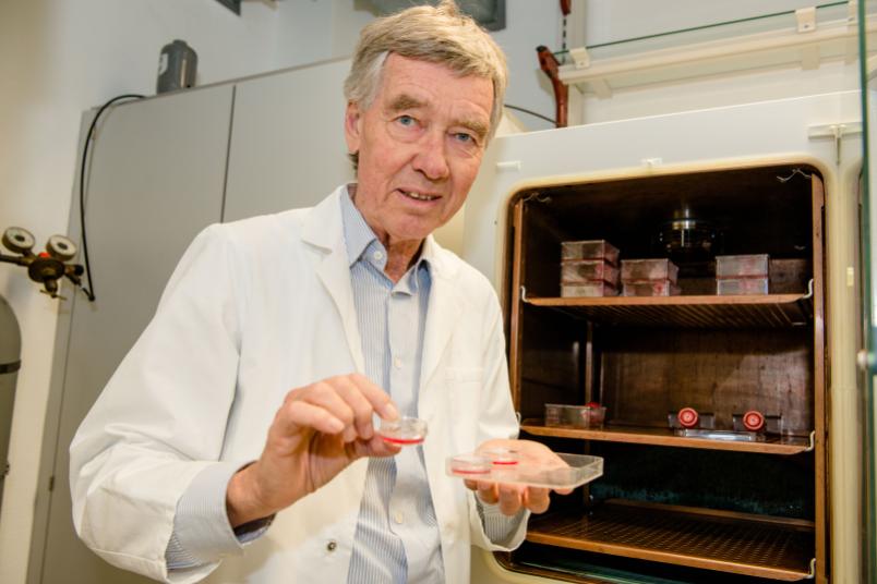 Ein Forscher vor einem Kühlschrank hält ein Schälchen in der Hand, in dem eine rote Flüssigkeit schwimmt