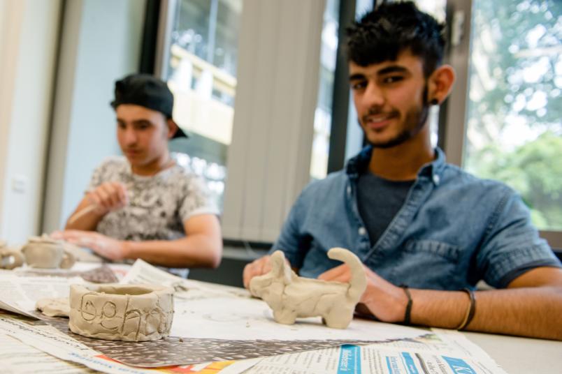 Schüler sitzt am Tisch und zeigt getöpferte Sachen.