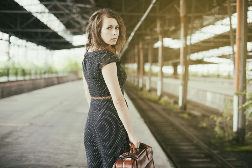 Katrin Hötzel steht mit einem Koffer in der Hand an einem Bahngleis.
