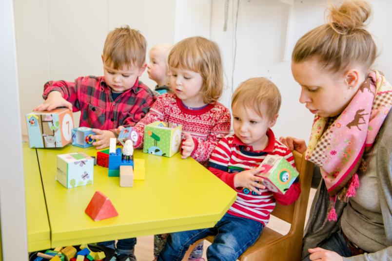 Drei Kleinkinder spielen zusammen mit einer Erzieherin.