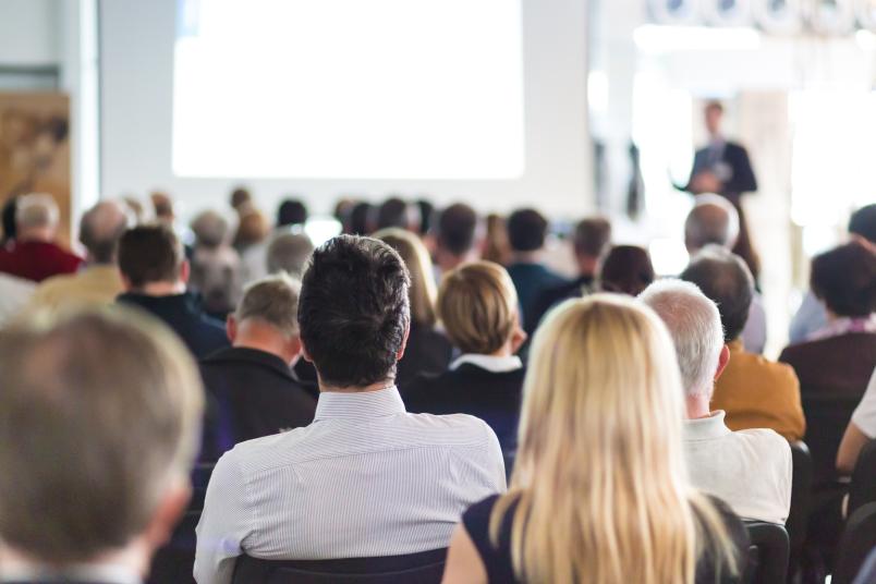 In einem Konferenzraum hören Tagungsteilnehmer einem Referenten zu.
