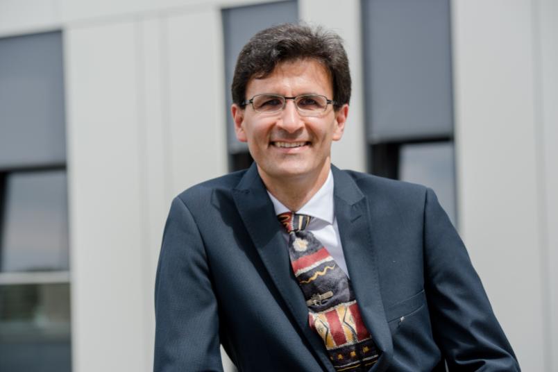 Mann mit Brille im Anzug, im Hintergrund das Unigebäude FNO