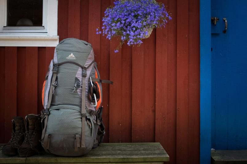 Ein Wanderrucksack steht auf einer Bank vor einem skandinavischen Haus.