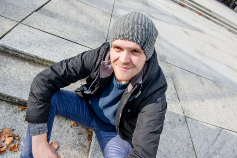Mann sitzt auf Steinboden und schaut nach oben in die Kamera.