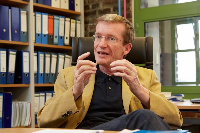 Mann sitzt am Schreibtisch und gestikuliert mit den Händen