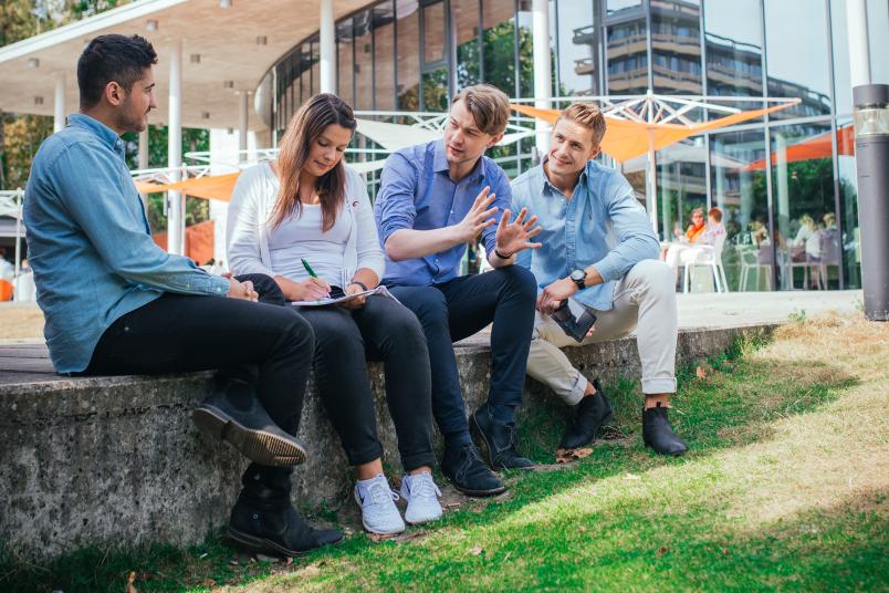 Vier Studierende unterhalten sich angeregt auf dem Campus.