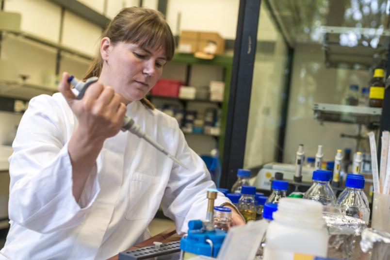 Eine Frau in weißem Kittel arbeitet im Labor mit einer Pipette.