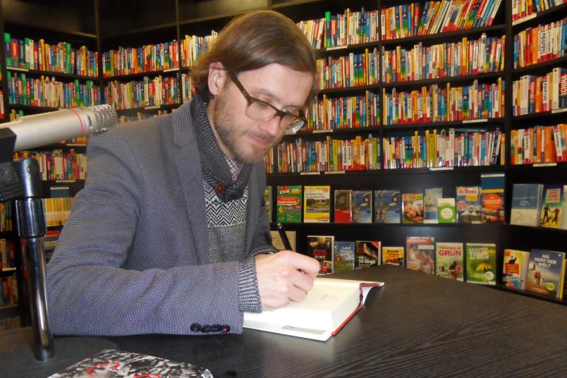 Junger Mann am Schreibtisch signiert ein Buch