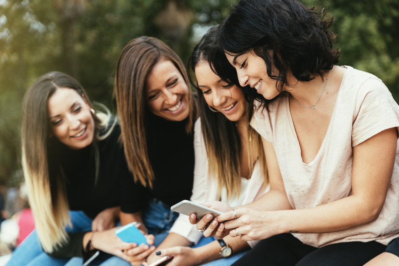 Vier junge Frauen schauen lachend auf ihre Smartphones.