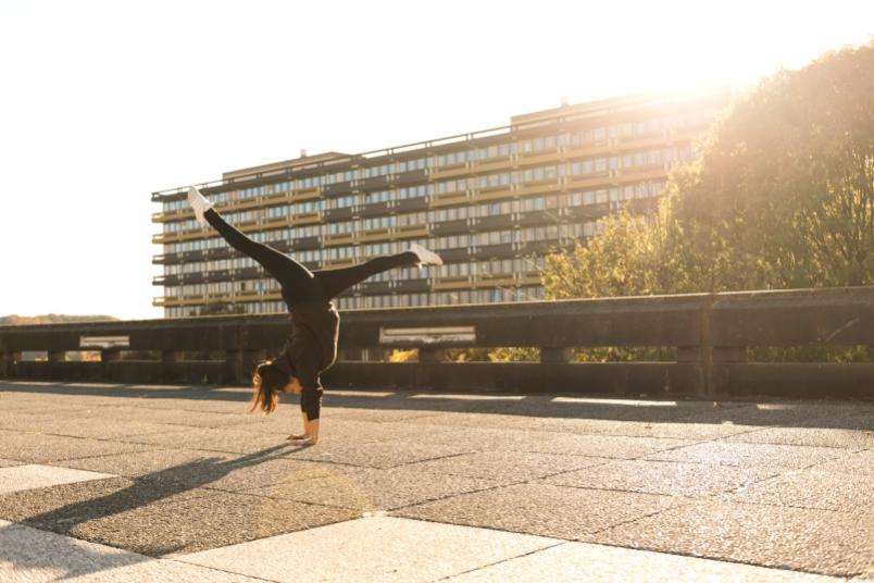 Eine Frau macht im Handstand Spagat im Freien vor dem GA-Gebäude. 